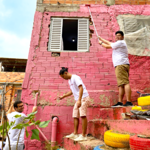 Foto de voluntários do Comitê Social da Perkins&Will, pintando uma parede de casa na cor rosa.